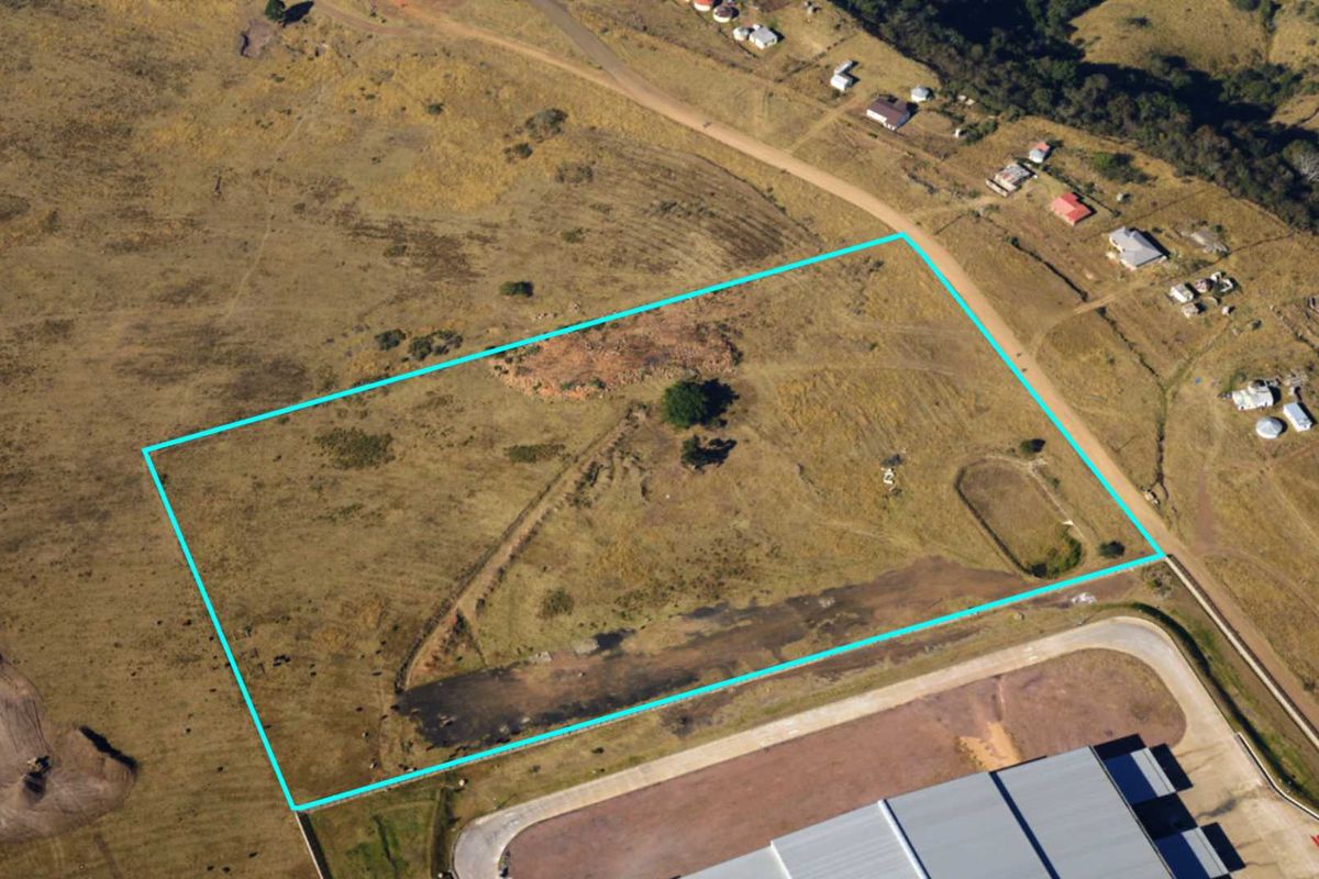 Aerial view of a vacant commercial land plot with clear boundary markings, situated in a developing area.
