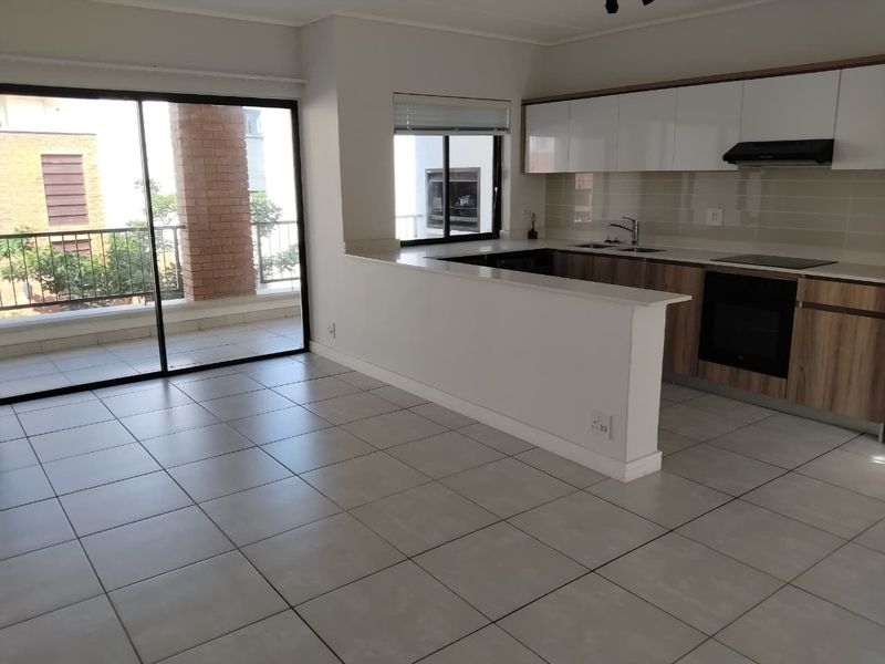 Modern open-plan kitchen and living area featuring sleek cabinetry, built-in appliances, tiled flooring, and direct access to a private balcony through sliding glass doors.