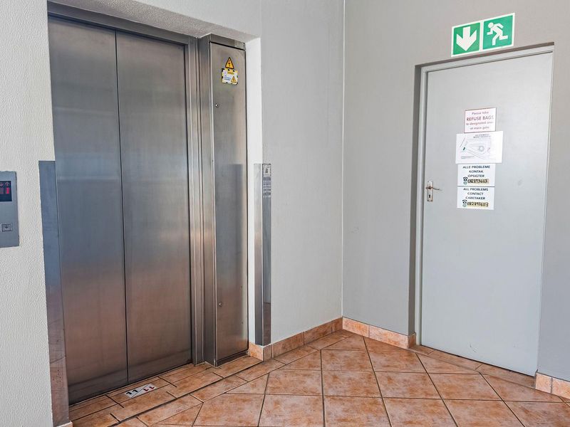 A clean, functional hallway area featuring a stainless steel elevator and a secure fire exit door with emergency signage.