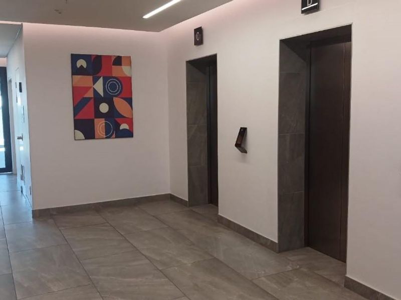 Modern office building lobby featuring a clean hallway with tiled flooring, recessed lighting, and dual elevator access.