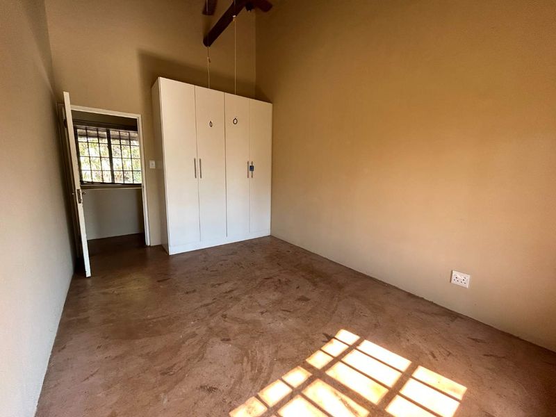 A vacant bedroom featuring a built-in wardrobe, exposed timber ceiling beam, and screeded concrete flooring with natural light.