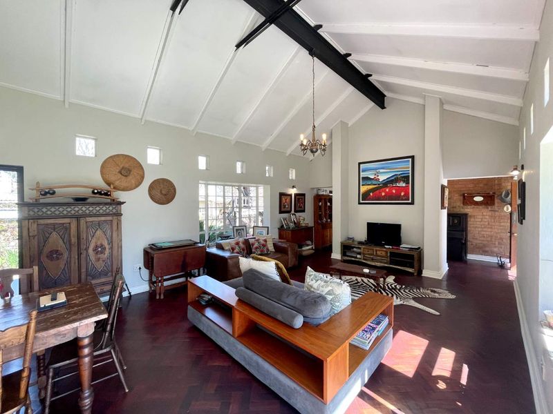 Spacious living room featuring a high vaulted ceiling with exposed steel beam, rich herringbone parquet flooring, and a characterful exposed brick accent wall.