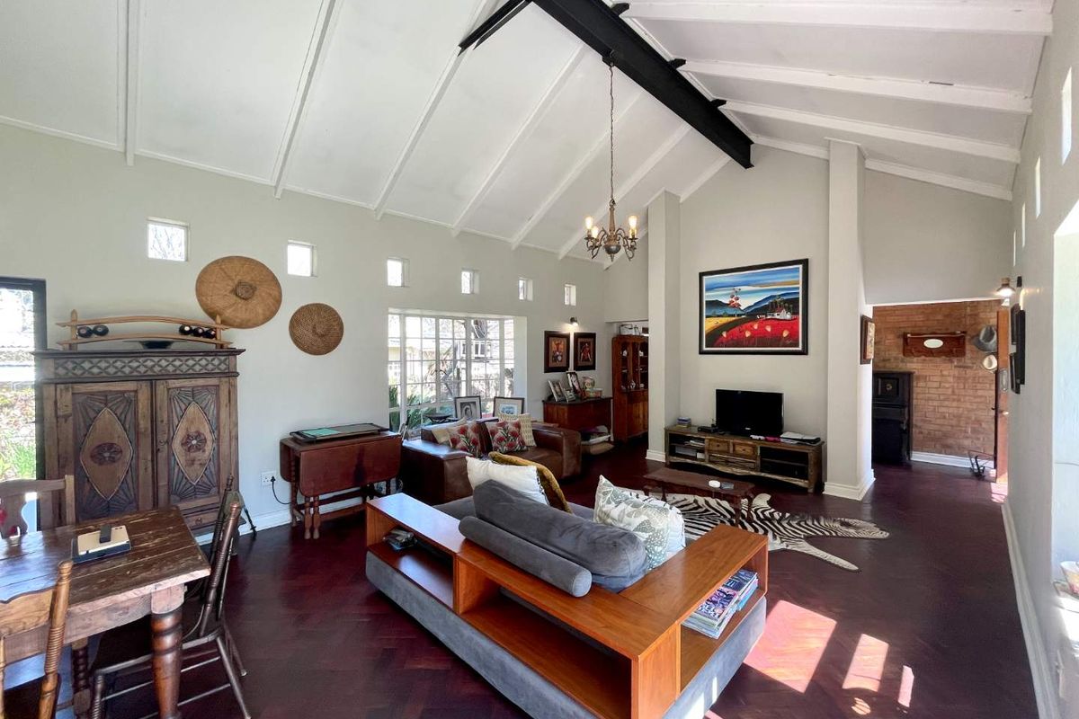 Spacious living room featuring a high vaulted ceiling with exposed steel beam, rich herringbone parquet flooring, and a characterful exposed brick accent wall.