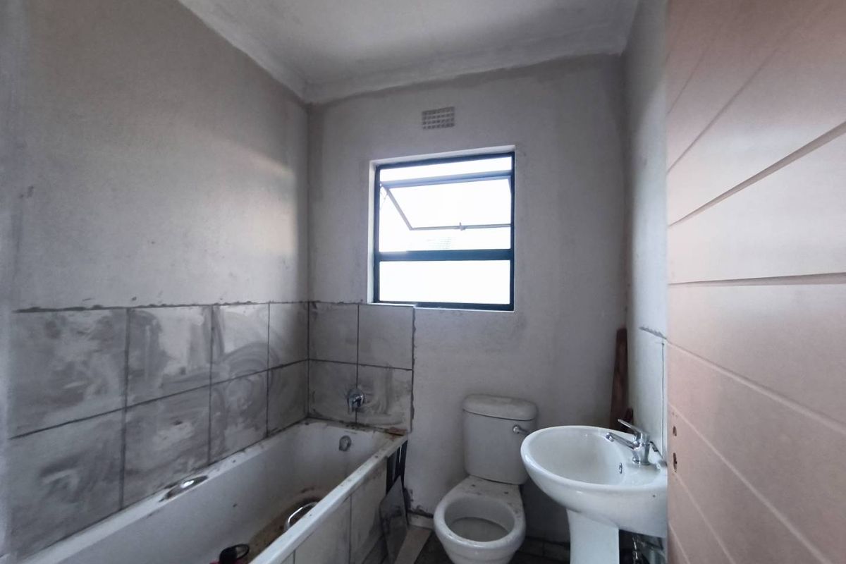 A bathroom in the process of renovation, featuring a bathtub, pedestal basin, and toilet, requiring completion of wall finishes and tiling.