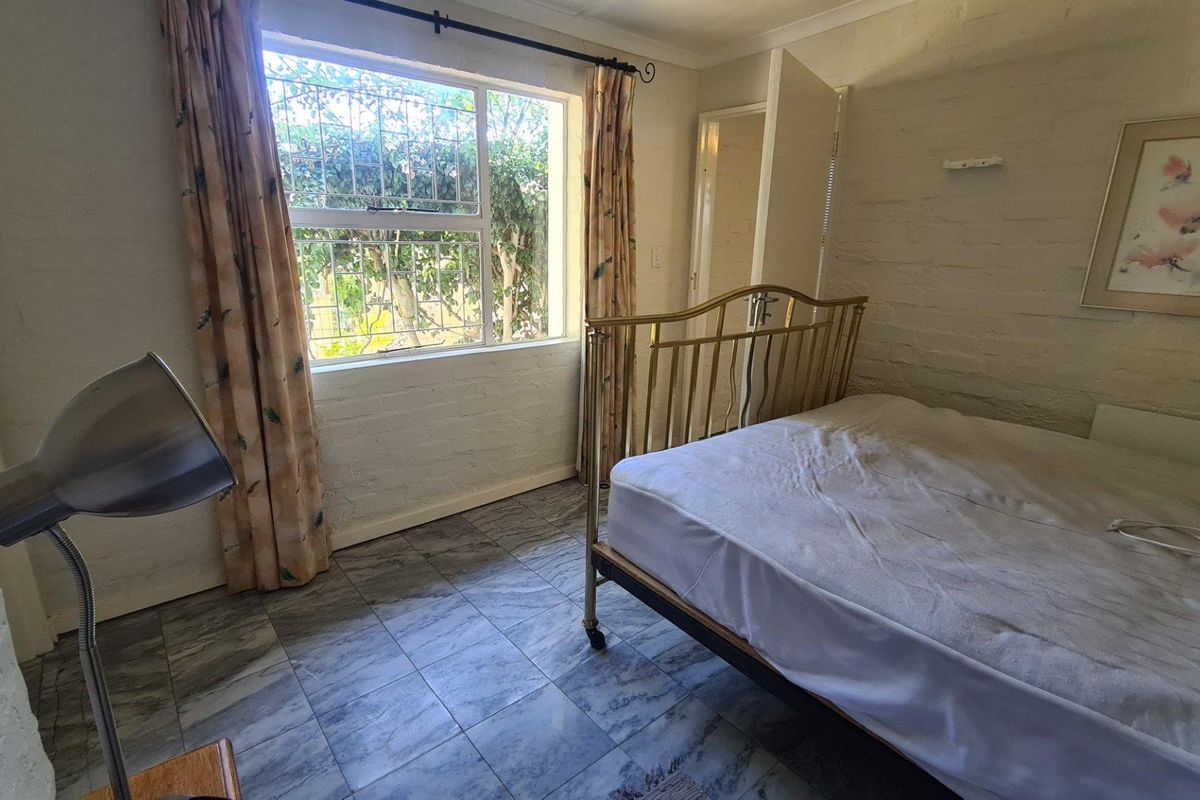 A bedroom featuring tiled flooring, painted brick walls, and a window with security bars, offering a functional space with potential for cosmetic updates.