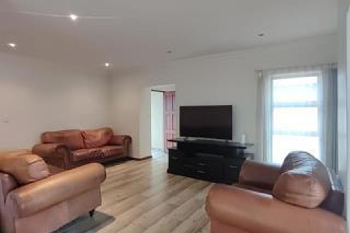 A spacious living room featuring light-toned laminate flooring, recessed ceiling lighting, and a large window allowing for natural light.