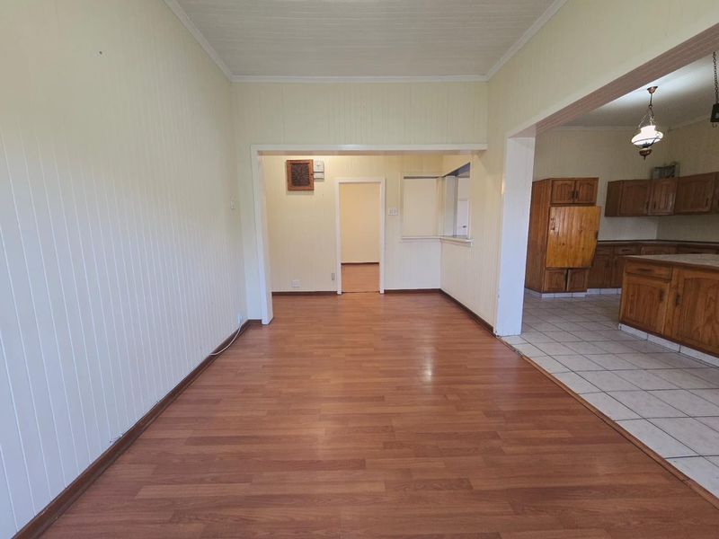 An open-plan living and kitchen area featuring laminate and tiled flooring, timber cabinetry, and a convenient kitchen pass-through window.