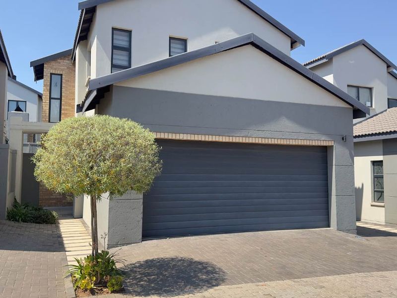 Front elevation of a modern townhouse featuring a double garage, paved driveway, and clean plastered facade with aluminium window frames.