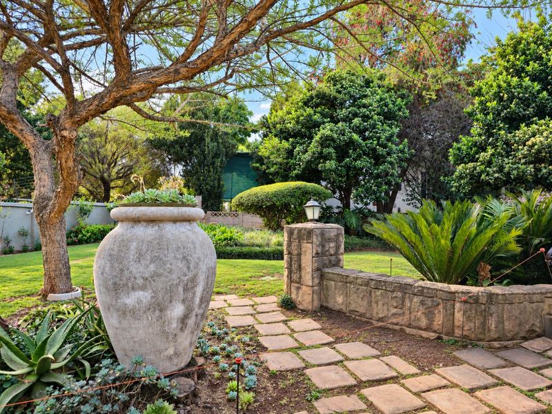 A well-maintained garden featuring a stone paver pathway, stone retaining wall, and mature landscaping with established trees and shrubs.