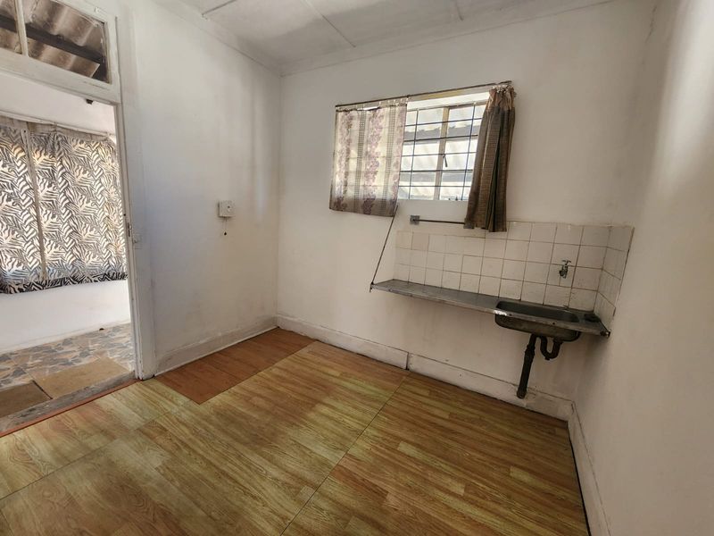 A basic scullery or utility area featuring a stainless steel sink, tiled splashback, and laminate flooring, requiring cosmetic updates.