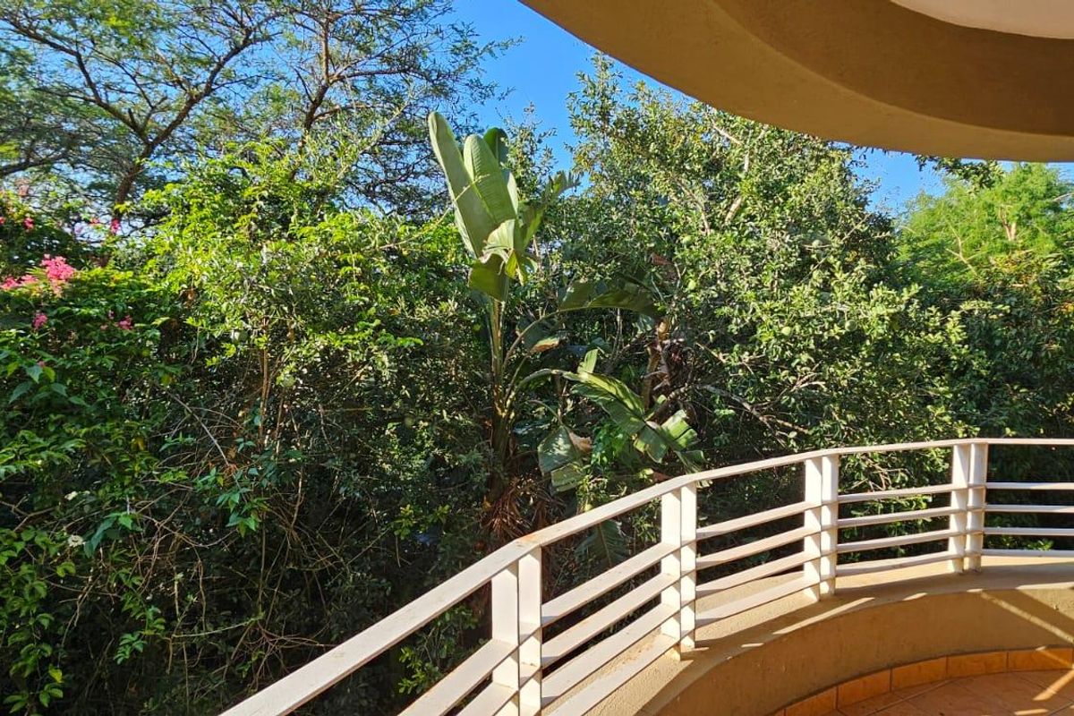 A private balcony featuring a metal balustrade and tiled flooring, offering a peaceful view of the surrounding lush greenery.
