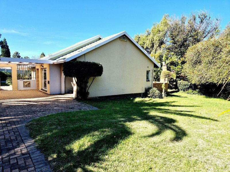 Rear view of the property featuring a paved driveway, covered patio area, and a well-maintained lawn with established garden surroundings.