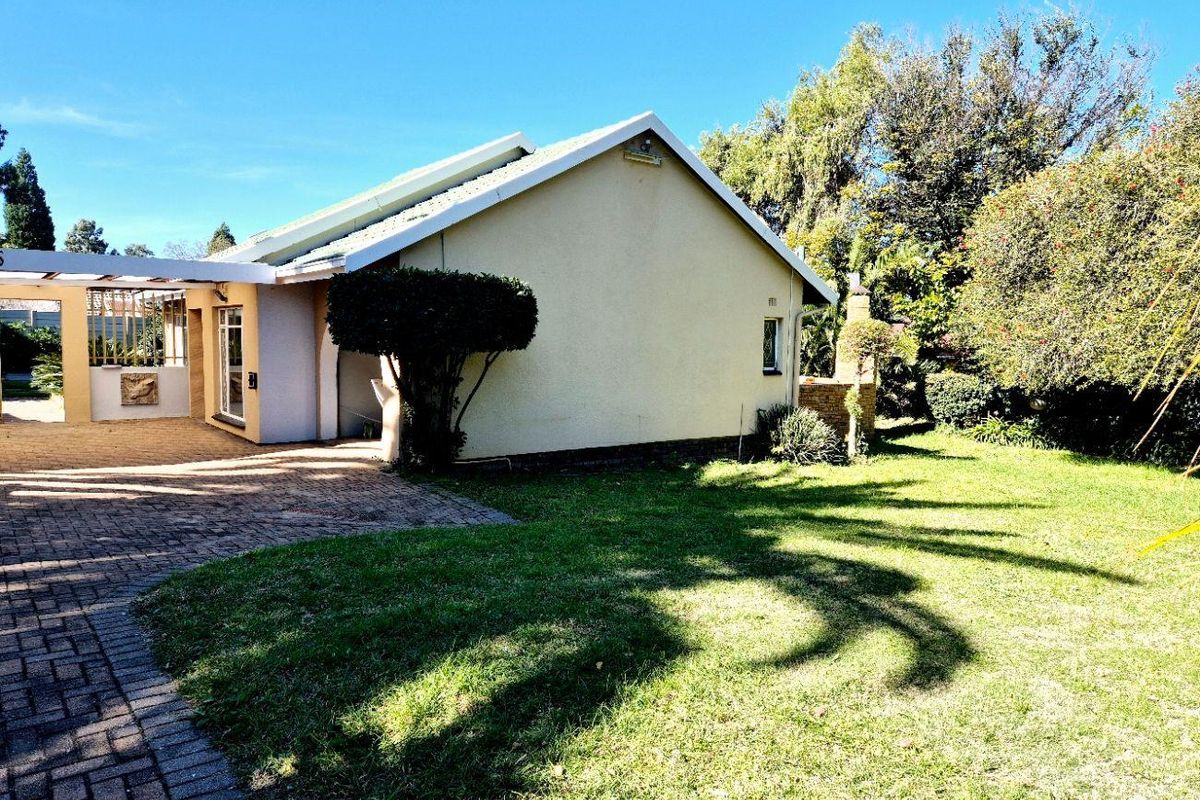 Rear view of the property featuring a paved driveway, covered patio area, and a well-maintained lawn with established garden surroundings.