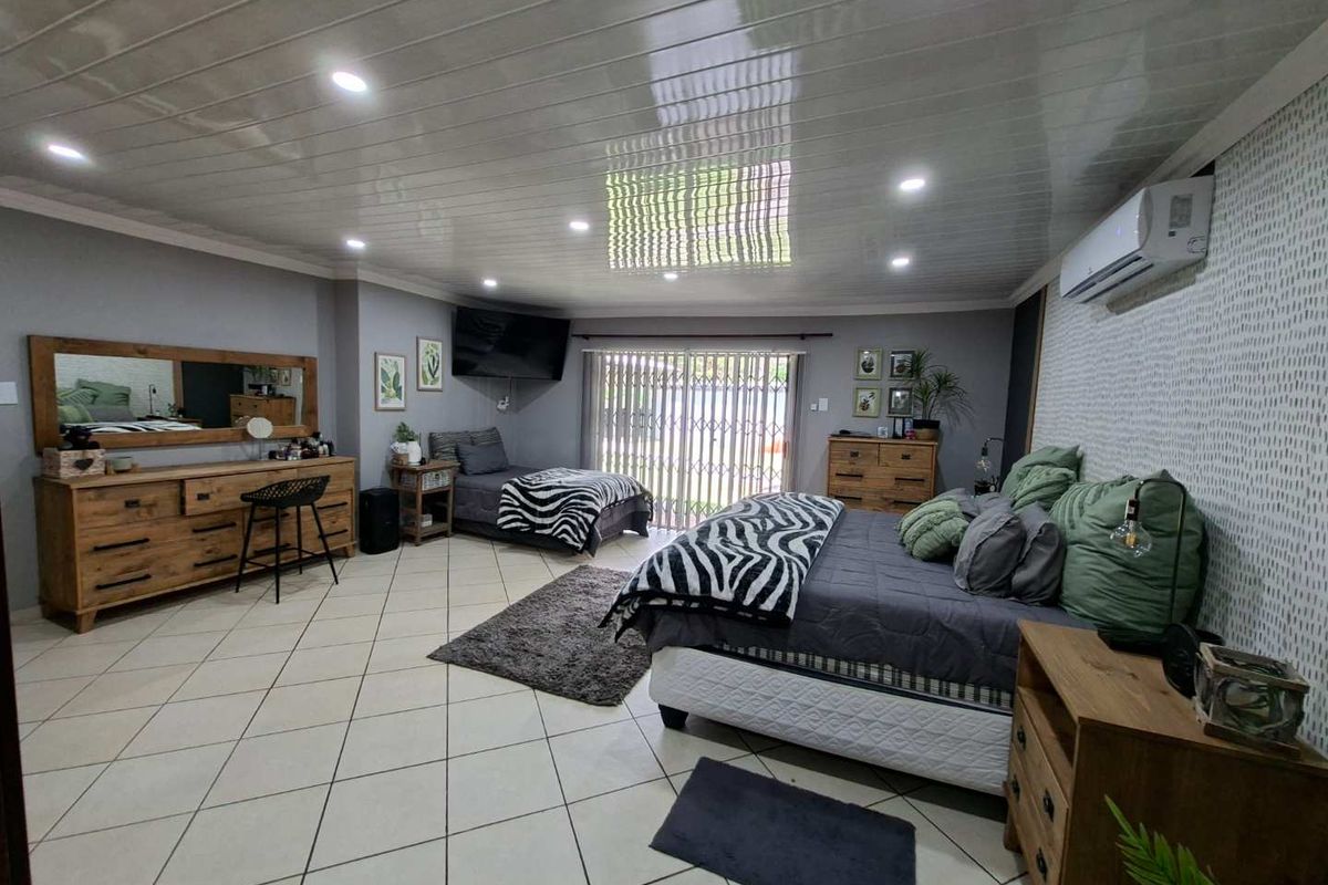 Spacious bedroom featuring tiled flooring, recessed ceiling lighting, a glossy panelled ceiling, and a wall-mounted air conditioning unit with sliding door access to the exterior.