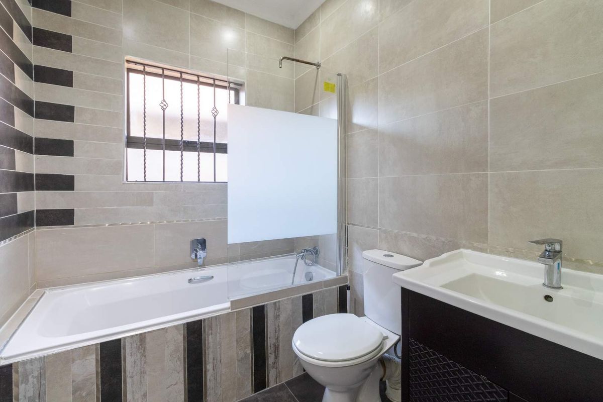 A modern bathroom featuring a built-in bathtub with a glass shower screen, a wall-mounted toilet, and a vanity basin with storage.