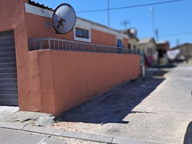 Street-facing view of a residential property featuring a boundary wall with security fencing, a garage entrance, and a mounted satellite dish.