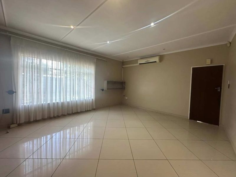 Spacious, empty living room featuring neutral tiled flooring, recessed ceiling lighting, and a wall-mounted air conditioning unit.