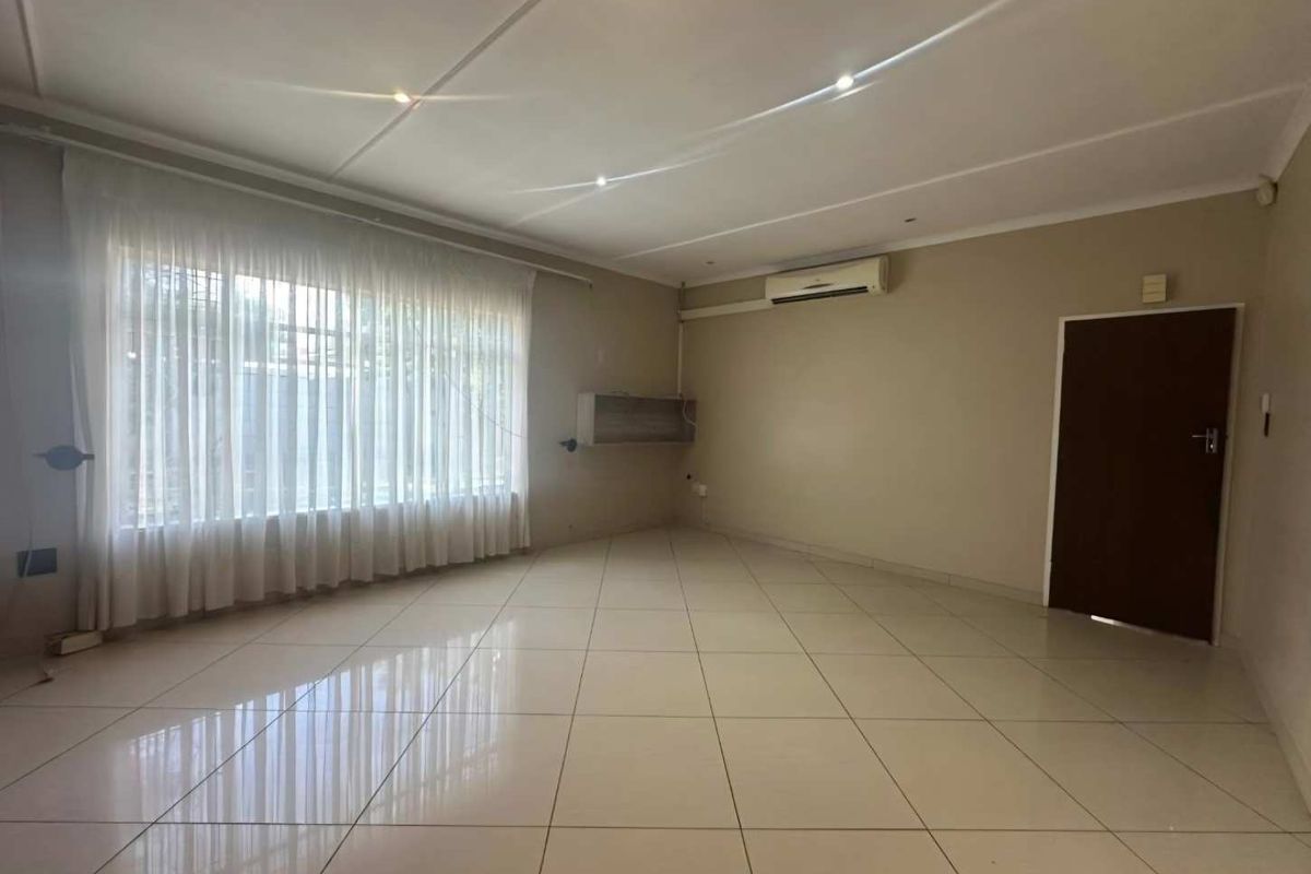 Spacious, empty living room featuring neutral tiled flooring, recessed ceiling lighting, and a wall-mounted air conditioning unit.