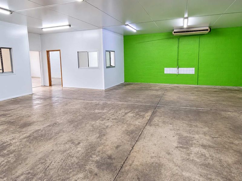 Spacious industrial utility area featuring durable concrete flooring, bright fluorescent lighting, and an integrated air conditioning unit, suitable for various commercial or storage uses.