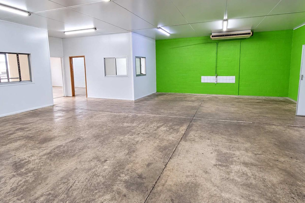 Spacious industrial utility area featuring durable concrete flooring, bright fluorescent lighting, and an integrated air conditioning unit, suitable for various commercial or storage uses.
