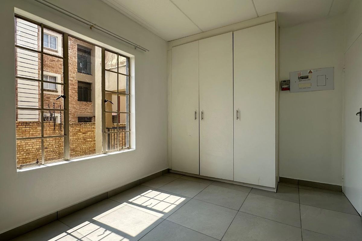 A bright, empty bedroom featuring neutral floor tiles, built-in white cabinetry, and large windows providing natural light.