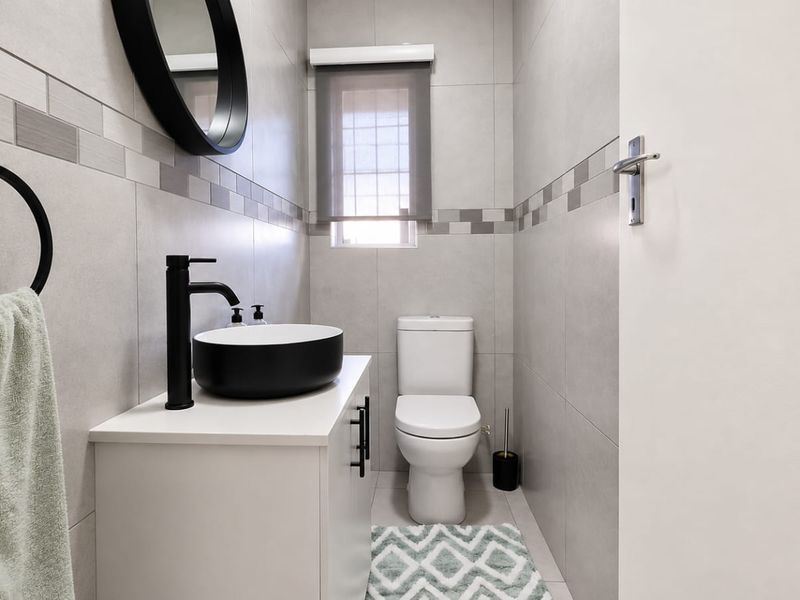 Modern guest bathroom featuring a sleek vanity with a vessel sink, black fixtures, and contemporary grey wall tiling.