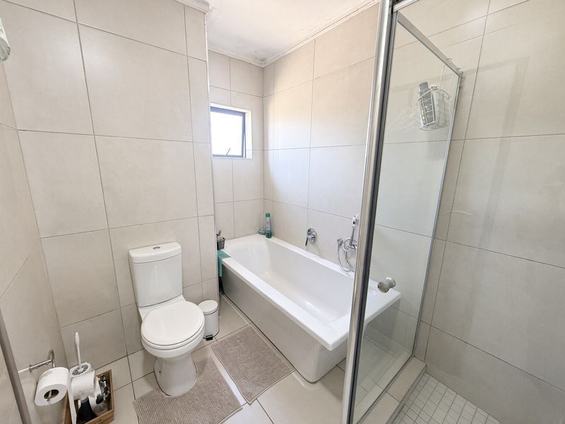 A functional bathroom featuring a bathtub, separate shower enclosure, and toilet, finished with neutral wall and floor tiling.