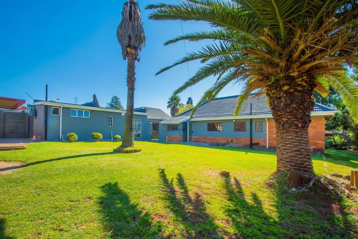A spacious rear garden featuring a well-maintained lawn, mature palm trees, and a view of the house's rear exterior facade.