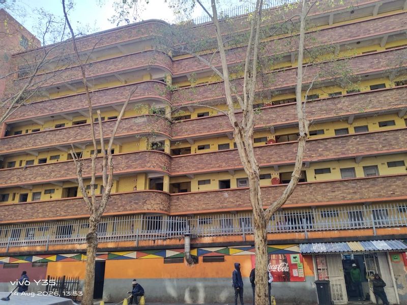 Exterior view of a multi-story apartment building featuring a brick facade, open balconies, and ground-level security fencing.
