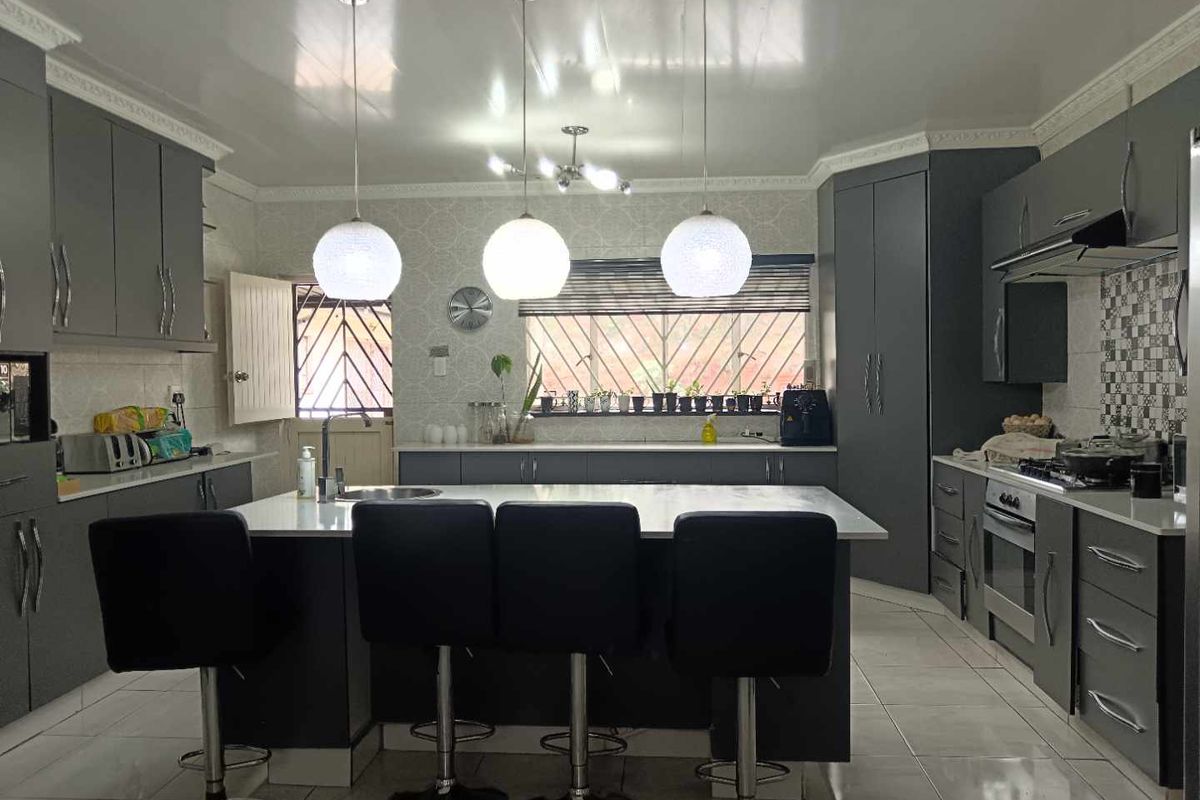 Modern kitchen featuring dark grey cabinetry, a central island with breakfast bar seating, stone countertops, and integrated stainless steel oven and extractor fan.