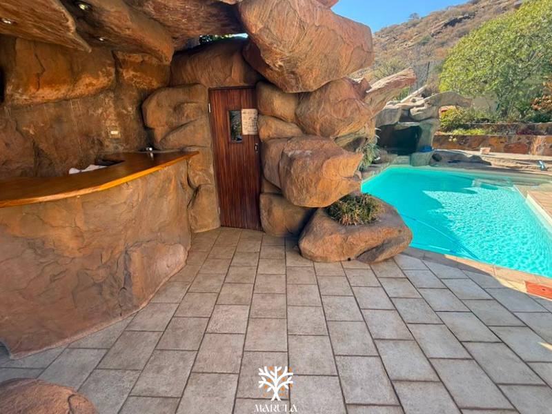 Outdoor entertainment area featuring a swimming pool, custom rock-feature bar, and tiled patio space, ideal for leisure and hosting.