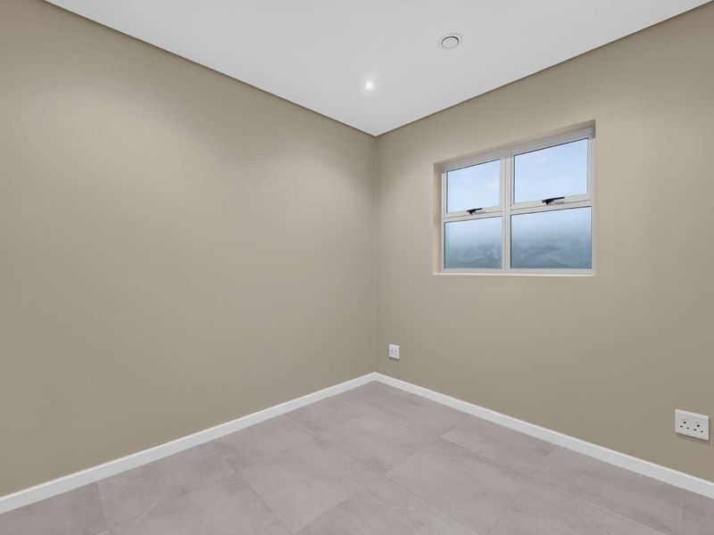 A clean, empty bedroom featuring neutral wall paint, modern grey floor tiles, recessed lighting, and a functional casement window.