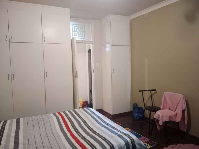 A bedroom featuring extensive white built-in cupboards, dark wooden flooring, and neutral wall tones, offering ample storage space.