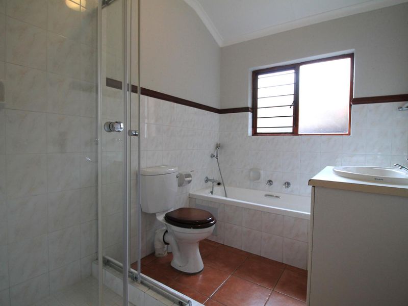 A functional bathroom featuring a shower enclosure, bathtub, toilet, and vanity basin with tiled finishes and a louvered window for ventilation.