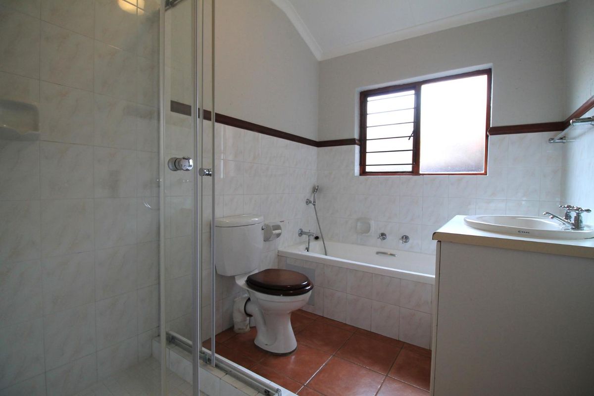 A functional bathroom featuring a shower enclosure, bathtub, toilet, and vanity basin with tiled finishes and a louvered window for ventilation.