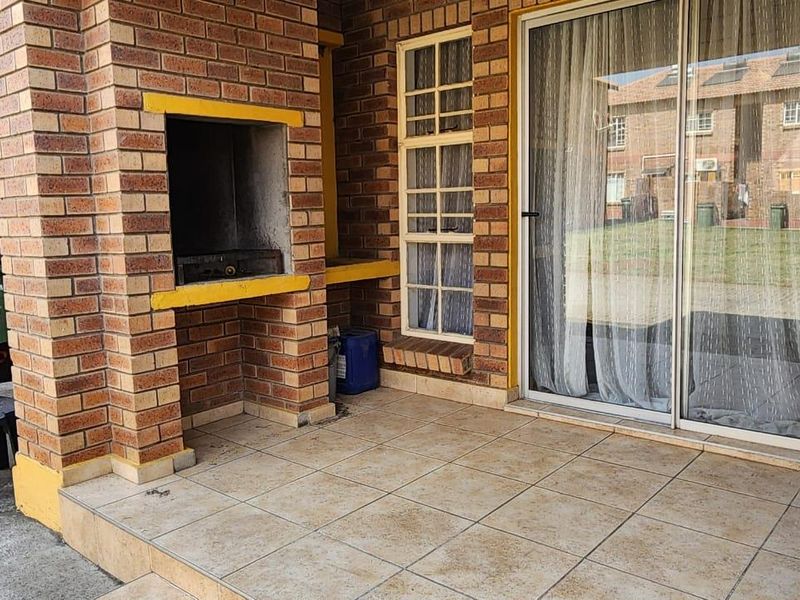 A paved patio area featuring a built-in brick braai and sliding glass door access to the apartment interior.