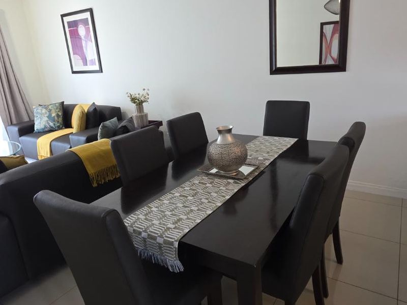 An open-plan living and dining area featuring neutral tiled flooring, clean white walls, and modern pendant lighting.