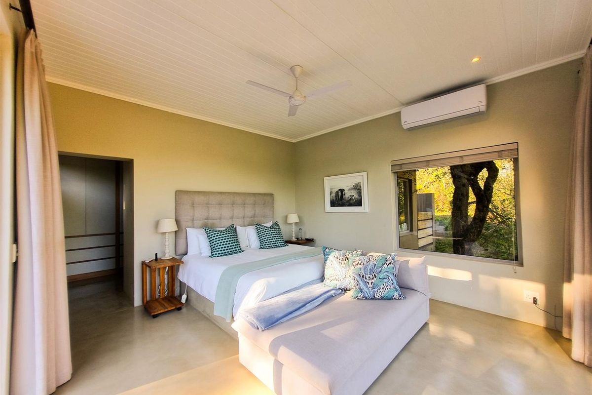 A well-maintained bedroom featuring a ceiling fan, split-system air conditioning, and large windows with natural views.