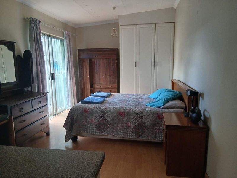 A bedroom featuring built-in wardrobes, laminate flooring, and sliding glass doors providing access to the exterior.