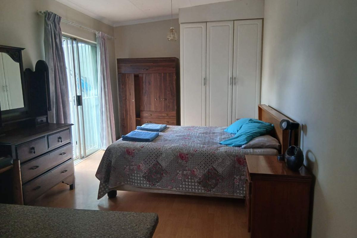 A bedroom featuring built-in wardrobes, laminate flooring, and sliding glass doors providing access to the exterior.