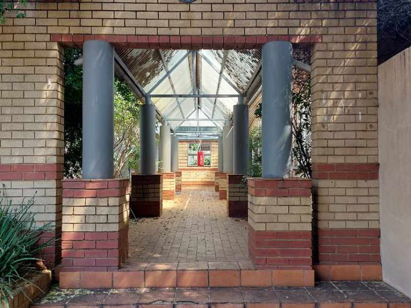 A covered brick entrance walkway featuring structural columns and a glass roof, leading to the main property access.