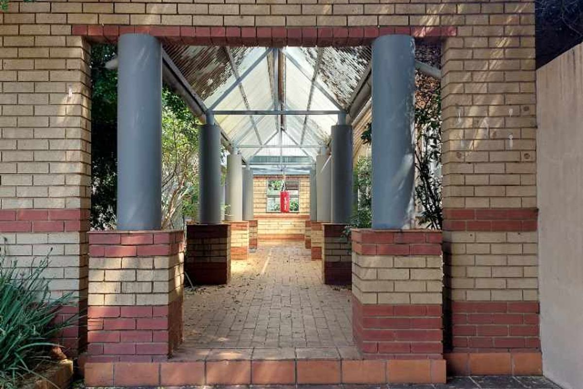 A covered brick entrance walkway featuring structural columns and a glass roof, leading to the main property access.