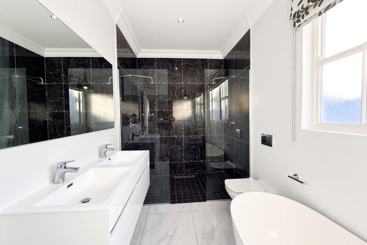 Modern bathroom featuring a double vanity, walk-in shower with black marble tiling, freestanding bathtub, and high-quality finishes throughout.