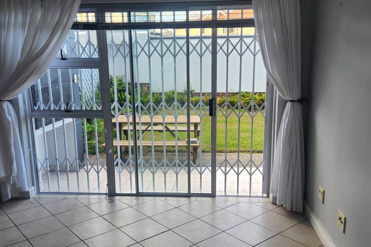 A bright living area featuring tiled flooring and a sliding glass door with a security gate, providing direct access to the rear garden.