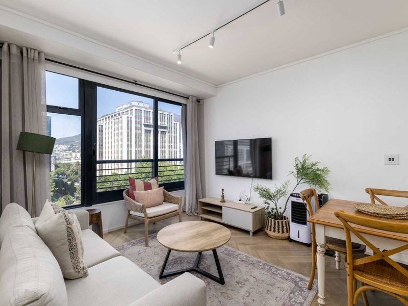 Bright open-plan living and dining area featuring herringbone parquet flooring, modern track lighting, and large windows with urban views.