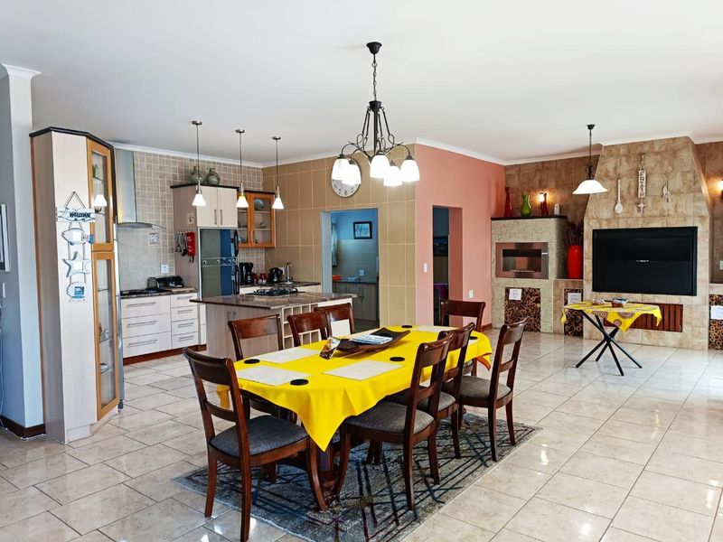 Spacious open-plan living and dining area featuring a modern kitchen with island, tiled floors, and a prominent stone-clad fireplace and built-in braai.