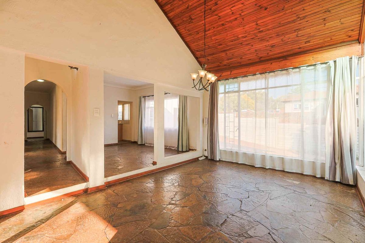 Spacious living area featuring a vaulted timber ceiling, unique flagstone flooring, and large windows that provide ample natural light.