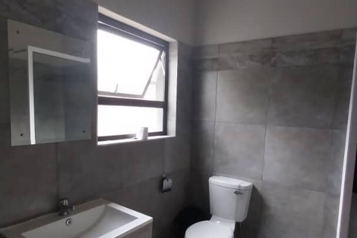 A modern bathroom featuring grey wall and floor tiles, a vanity with a basin, a toilet, and a window for natural light.