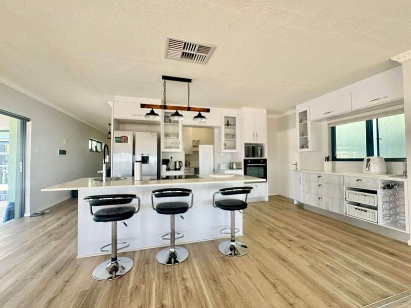 Modern kitchen featuring a central island, built-in appliances, white cabinetry, and light wood-look laminate flooring in an open-plan layout.