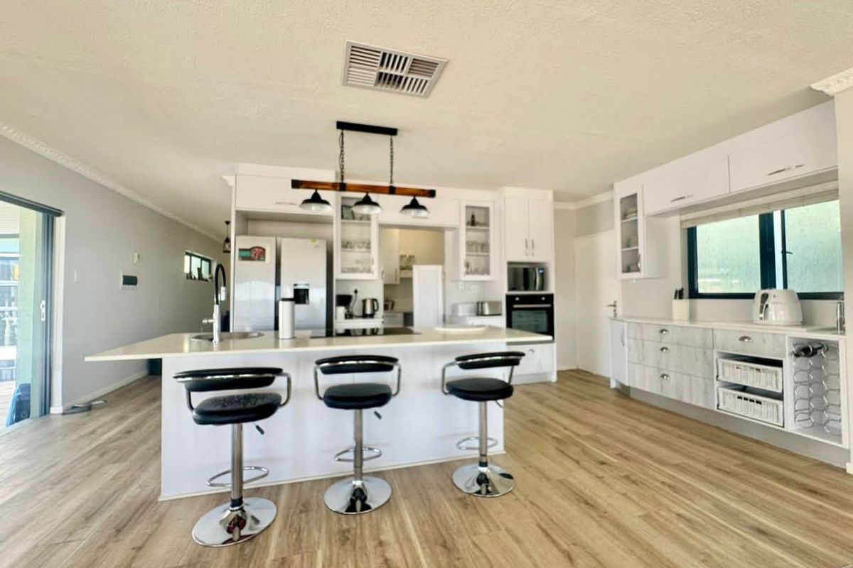 Modern kitchen featuring a central island, built-in appliances, white cabinetry, and light wood-look laminate flooring in an open-plan layout.